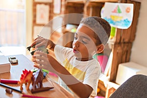 Beautiful african american toddler playing with dinosaurs toy on desk at kindergarten