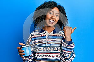 Beautiful african american woman with afro hair drinking a cup of coffee pointing thumb up to the side smiling happy with open