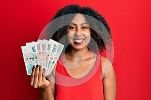 Beautiful african american woman with afro hair holding czech koruna banknotes looking positive and happy standing and smiling