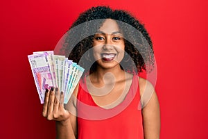Beautiful african american woman with afro hair holding indian rupee banknotes looking positive and happy standing and smiling
