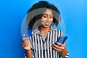 Beautiful african american woman with afro hair holding smartphone and credit card smiling with a happy and cool smile on face