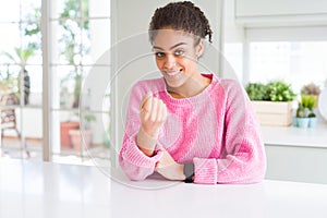 Beautiful african american woman with afro hair wearing casual pink sweater Beckoning come here gesture with hand inviting