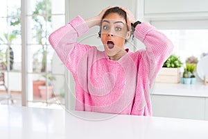 Beautiful african american woman with afro hair wearing casual pink sweater Crazy and scared with hands on head, afraid and