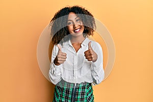 Beautiful african american woman with afro hair wearing scholar skirt success sign doing positive gesture with hand, thumbs up