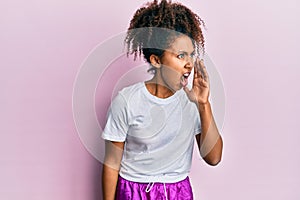 Beautiful african american woman with afro hair wearing sportswear shouting and screaming loud to side with hand on mouth