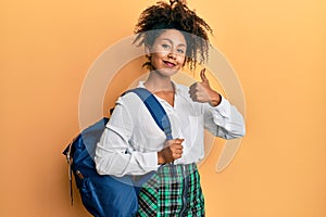 Beautiful african american woman with afro hair wearing student backpack smiling happy and positive, thumb up doing excellent and