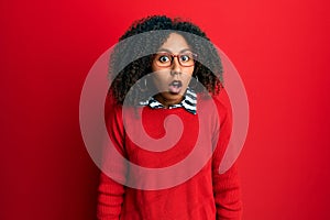 Beautiful african american woman with afro hair wearing sweater and glasses afraid and shocked with surprise and amazed
