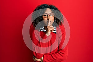 Beautiful african american woman with afro hair wearing sweater and glasses asking to be quiet with finger on lips