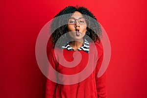 Beautiful african american woman with afro hair wearing sweater and glasses making fish face with lips, crazy and comical gesture