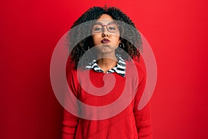 Beautiful african american woman with afro hair wearing sweater and glasses puffing cheeks with funny face