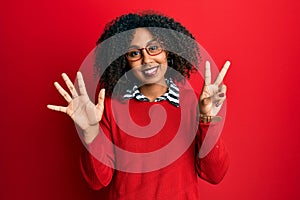Beautiful african american woman with afro hair wearing sweater and glasses showing and pointing up with fingers number seven