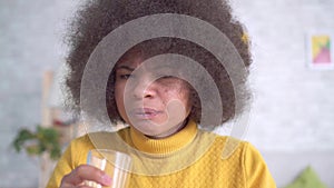 Beautiful african american woman with an afro hairstyle takes a pill and drinks from a glass of water