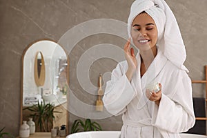 Beautiful African American woman applying cream onto face in bathroom, space for text