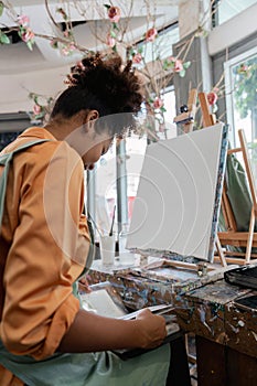 Beautiful African american woman artist confident painting on canvas at art studio