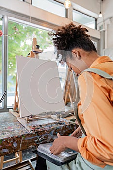 Beautiful African american woman artist confident painting on canvas at art studio