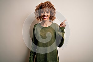 Beautiful african american woman with curly hair wearing casual sweater over white background with a big smile on face, pointing