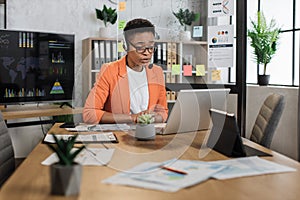 Beautiful african american woman in formal clothes sitting at desk and typing on wireless laptop.