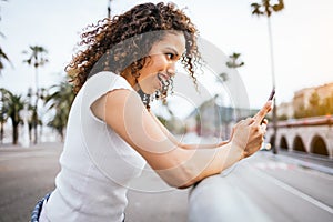Beautiful African-American woman happily sending text messages through mobile phone