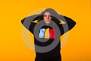 Beautiful African American woman having fun in black sweatshirt on a yellow background. Street fashion photo with afro