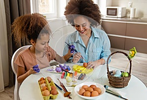 Beautiful African American woman and her daughter coloring Easter eggs
