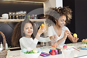 Beautiful African American woman and her daughter coloring Easter eggs in the kitchen