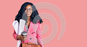 Beautiful african american woman holding paper blueprints and drinking coffee looking positive and happy standing and smiling with