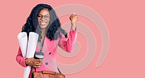 Beautiful african american woman holding paper blueprints and drinking coffee screaming proud, celebrating victory and success