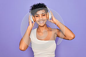 Beautiful african american woman listening to music using headphones over red background with a happy face standing and smiling