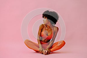 beautiful African american woman meditating in sports outfit on pink background