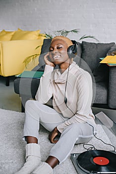 Beautiful african american woman sitting on carpet and listening music