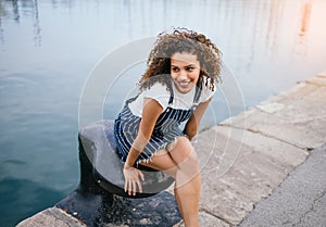 Beautiful African-American woman sitting on a mooring beside a lake