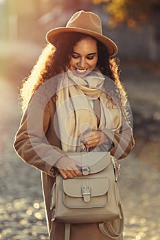 Beautiful African-American woman with stylish beige backpack on autumn day