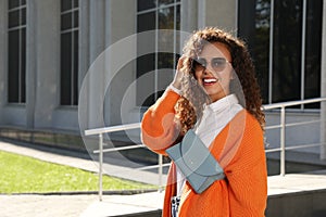 Beautiful African American woman with stylish waist bag on city street, space for text