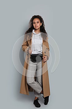 Beautiful African American woman with stylish waist bag on grey background