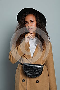 Beautiful African American woman with stylish waist bag on grey background