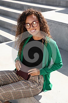 Beautiful African American woman with stylish waist bag on stairs outdoors