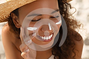 Beautiful African American woman with sun protection cream on face at sandy beach, closeup