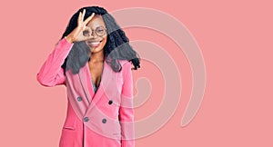 Beautiful african american woman wearing business jacket and glasses smiling happy doing ok sign with hand on eye looking through