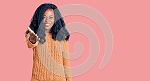 Beautiful african american woman wearing casual  sweater smiling friendly offering handshake as greeting and welcoming