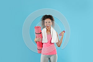 Beautiful African American woman with yoga mat, towel and dumbbell on turquoise background