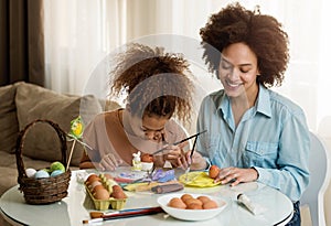 Beautiful African American woman and her daughter coloring Easter eggs