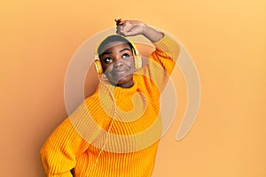 Beautiful african american young woman with short hair wearing headphones listening to music and dancing over isolated yellow