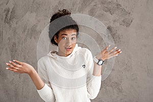 Beautiful african girl shruging, looking at camera over beige background.