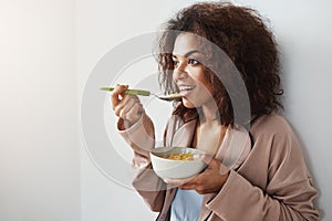 Beautiful african girl in sleepwear smiling eating flakes with milk at home. Copy space.
