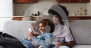 Beautiful African teenage couple relaxing on sofa with gadget