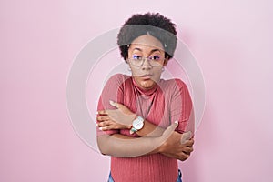 Beautiful african woman with curly hair standing over pink background shaking and freezing for winter cold with sad and shock