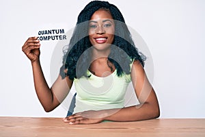 Beautiful african woman holding quantum computer banner looking positive and happy standing and smiling with a confident smile