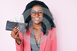 Beautiful african woman holding wallet with dollars looking positive and happy standing and smiling with a confident smile showing