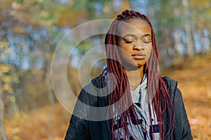 Beautiful african woman with long red hair and closed eyes. Close-up portrait. Autumn park location.