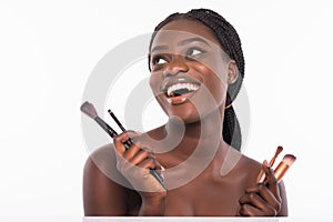Beautiful african woman with makeup brushes near her face isolated on white background